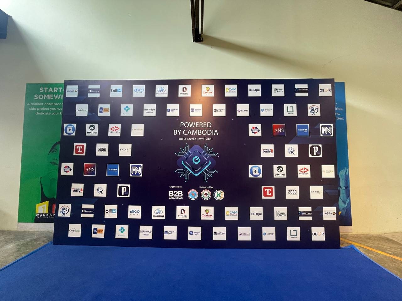 The Powered by Cambodia exhibitor wall, showing the campaign tagline Build Local, Grow Global